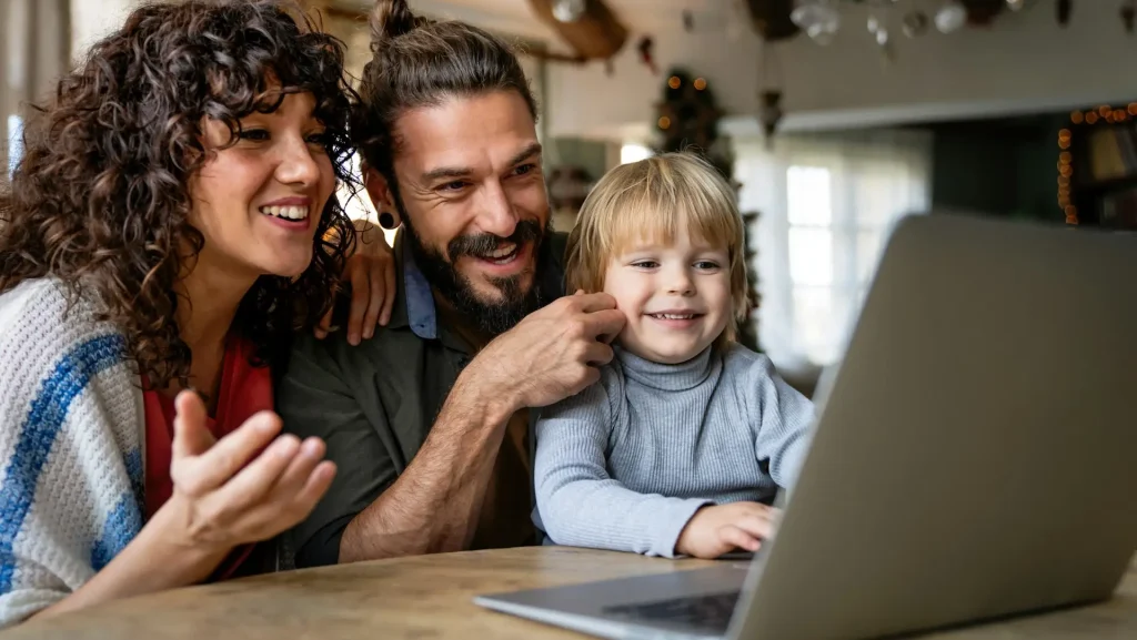 Happy family with kid having fun using laptop together, watching internet video, making online call